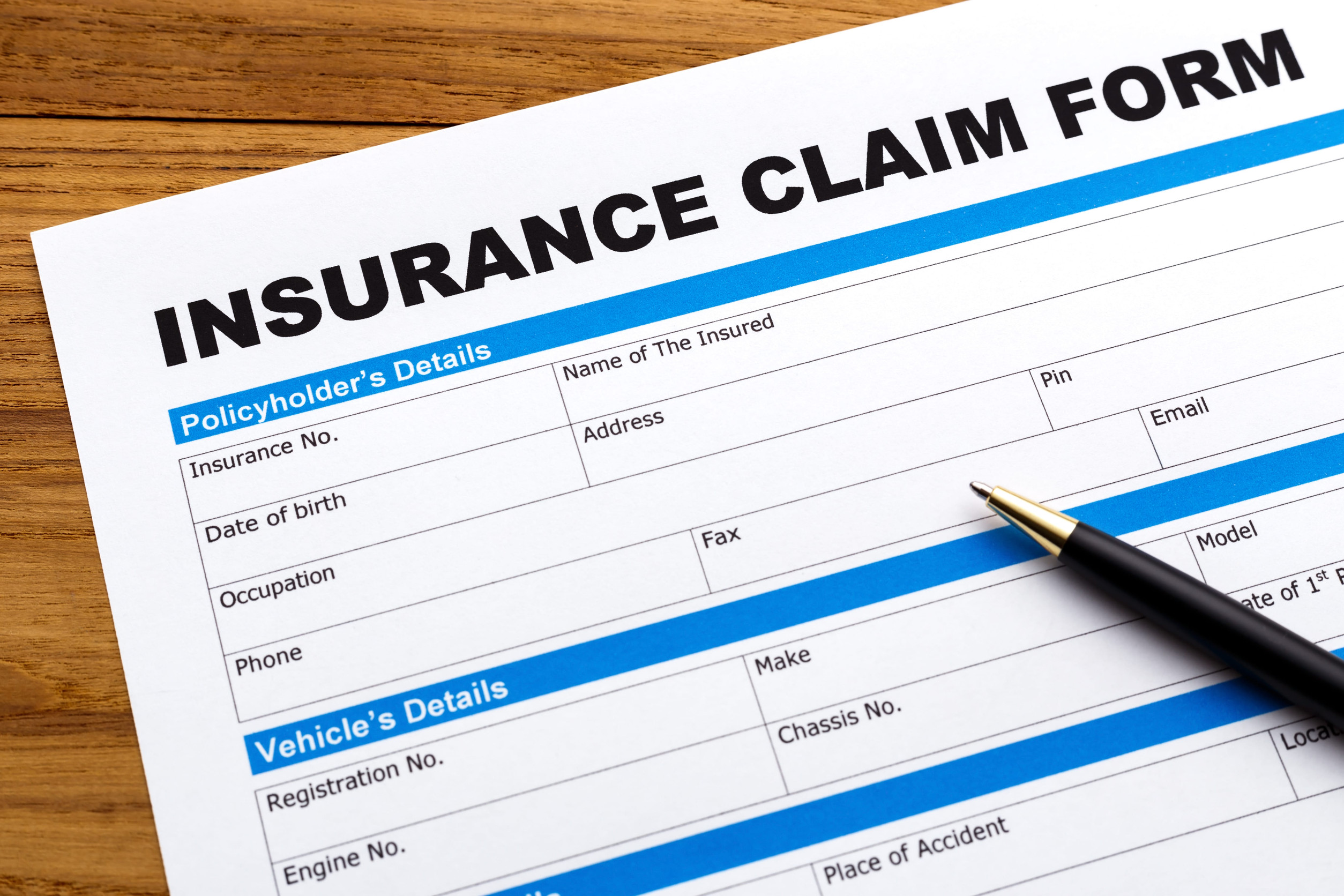 A close-up of a Central MN insurance claim form on a wooden surface with a black pen placed on the form, ready to be filled out. The form includes fields for policyholder and vehicle details.