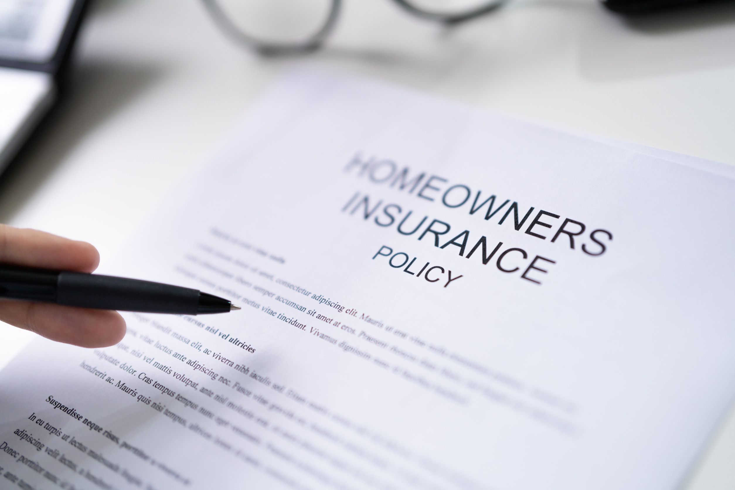 A hand holds a pen over a Homeowners Insurance Policy, illustrating common home insurance mistakes to avoid.